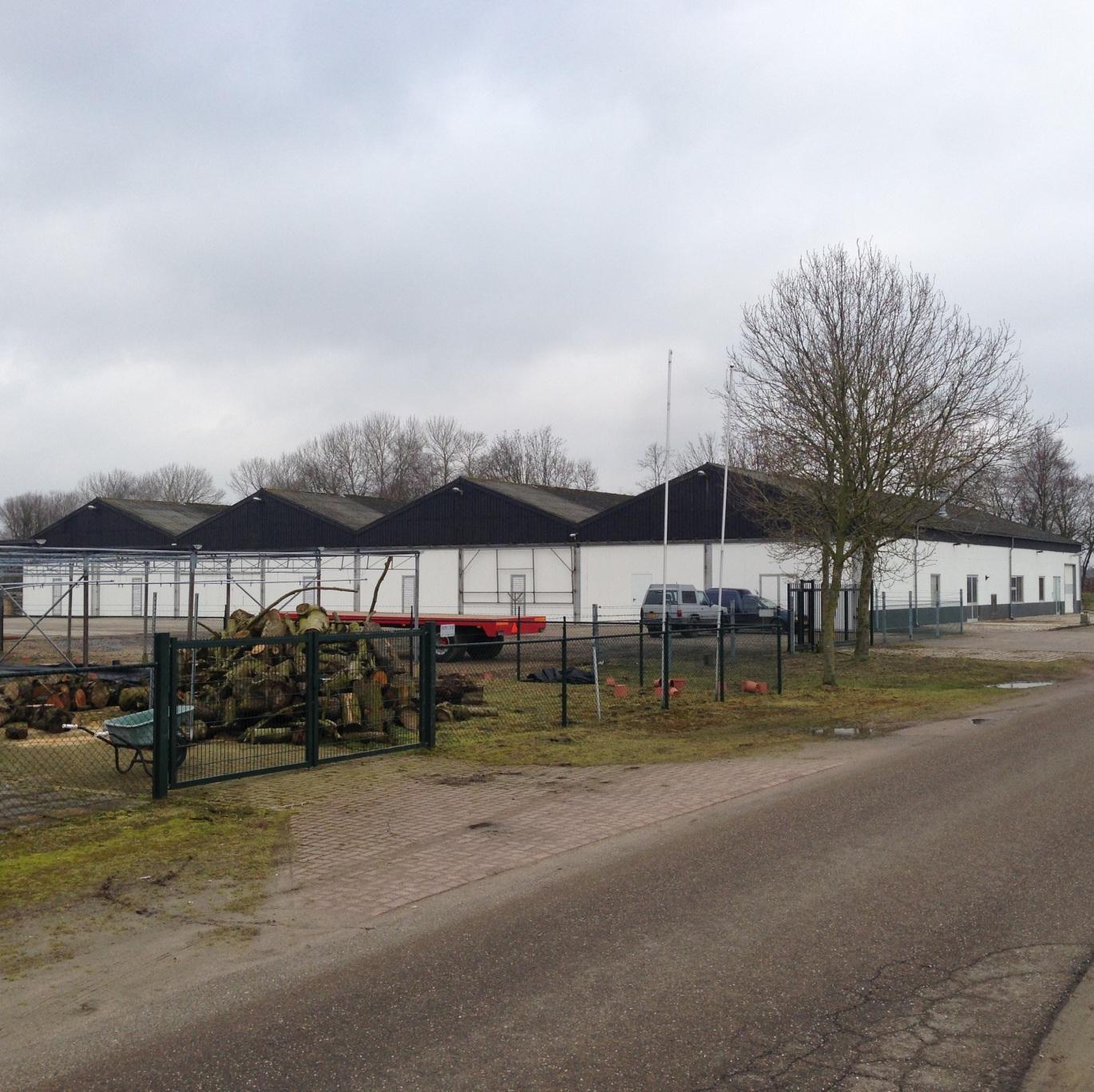 De opslagloods met zwarte daken en witte gevel, vanaf de weg
