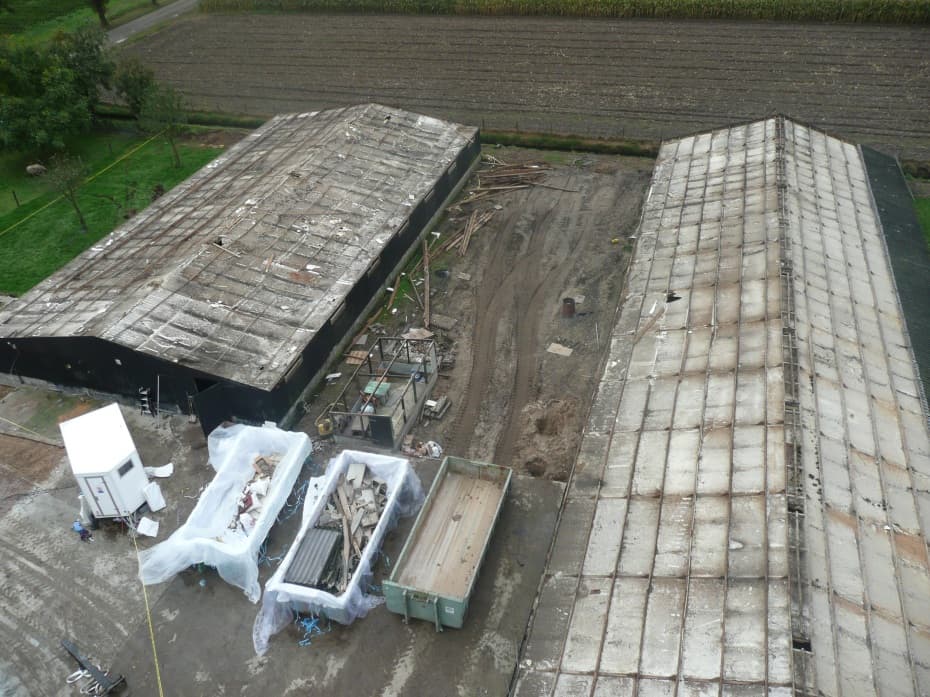 Luchtfoto van de sloop van de oude kippenstallen, containers vol puin