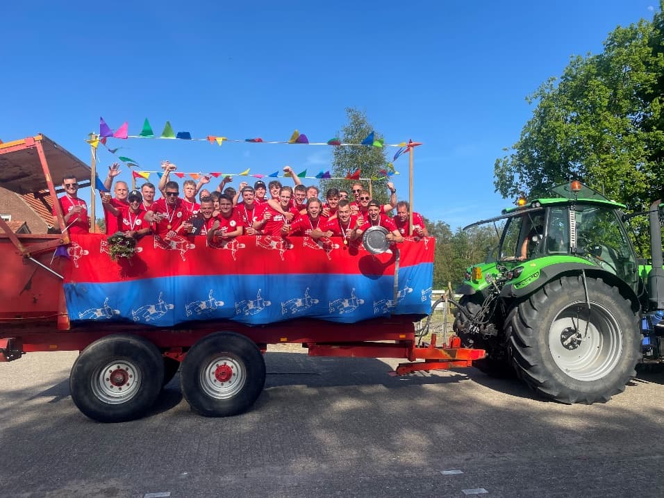 Voetbalteam in rode shirts met schaal op een boerenwagen achter de Deutz