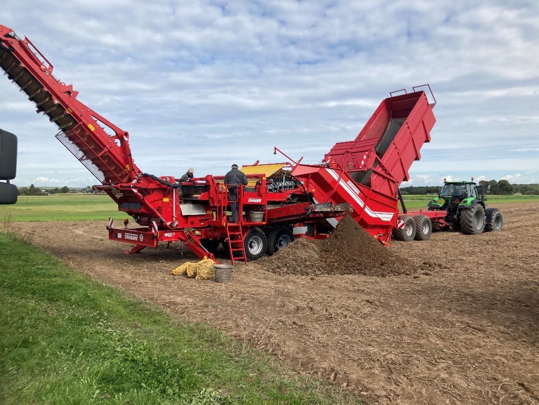 Aardappelrooier op de akker met mensen op de machine