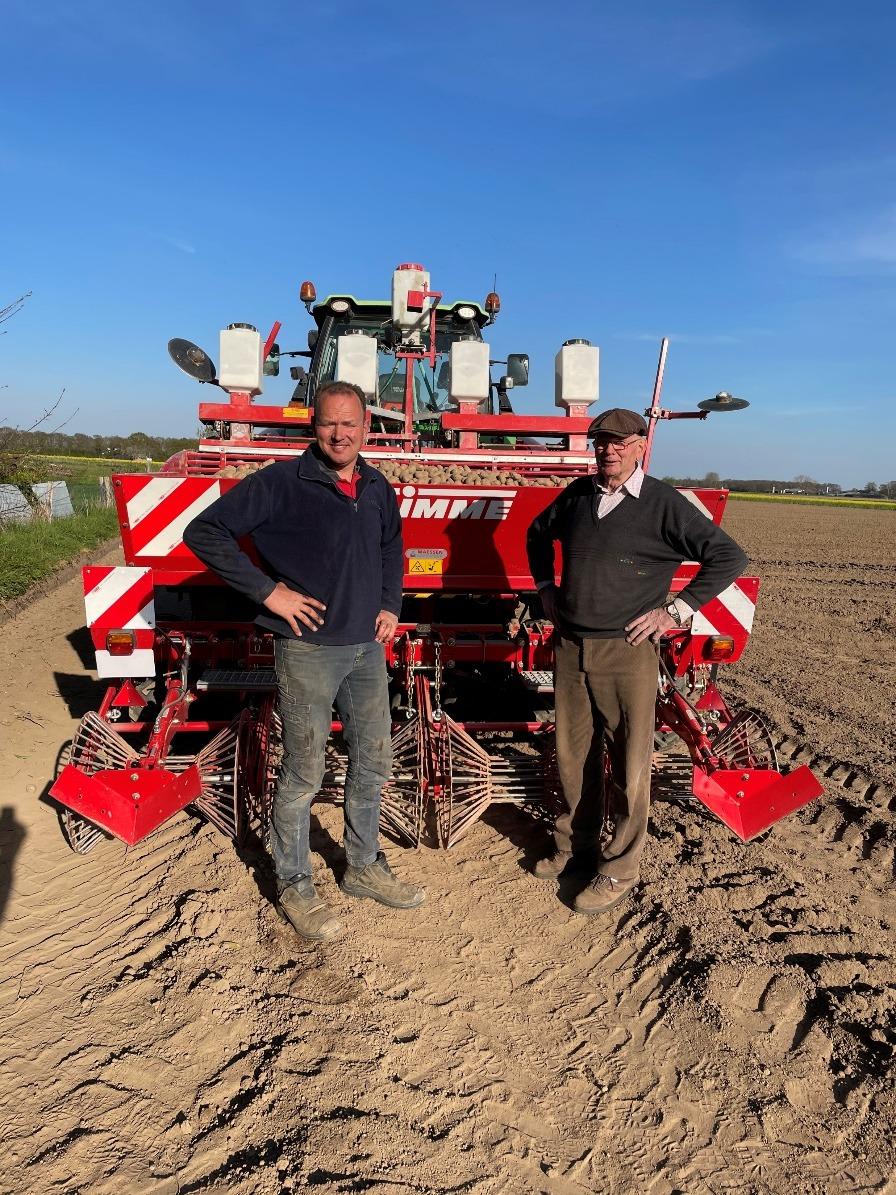 Twee mannen voor de pootmachine onder een blauwe lucht